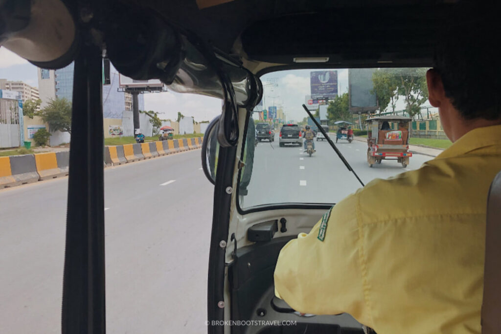 Sitting in the back of a Tuk Tuk on a busy road with driver wearing yellow shirt
