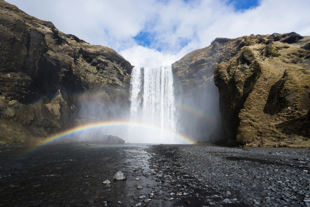 waterfall in iceland in front of a blue sky with a rainbow