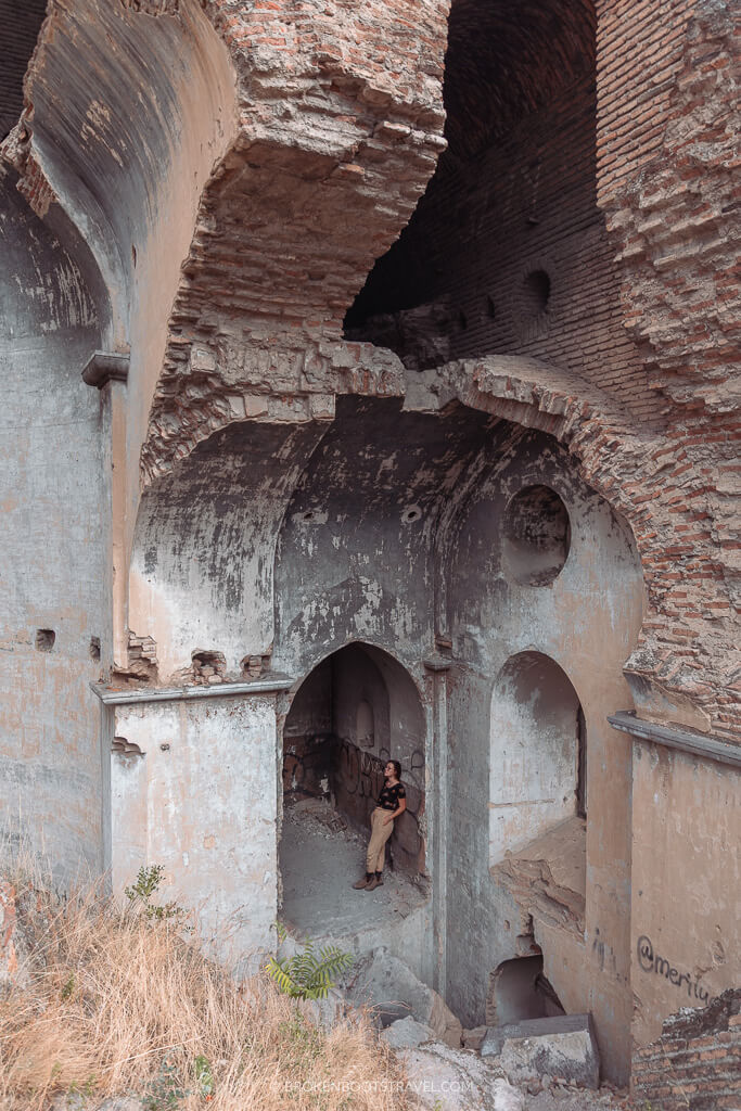 A girl stands in an archway of an abandoned building