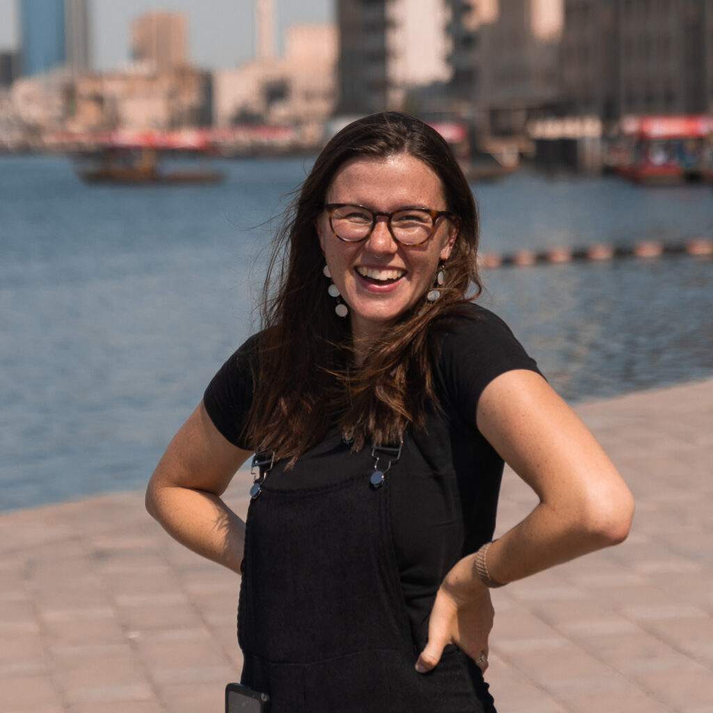 Girl in black overalls smiling in front of river and buildings