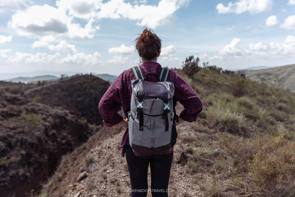 Girl in red shift wearing a backpack and looking out at green mountains