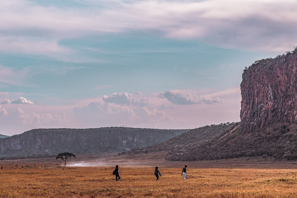 People walking across a field with a cliff in the background