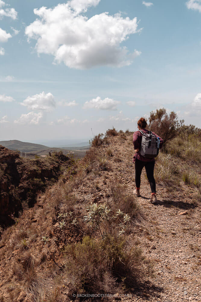 Girl walking along the rim of a volcano wearing a brown backpack