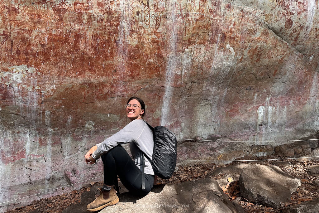 Girl in blue shirt and black leggings smiling in front of rock paintings