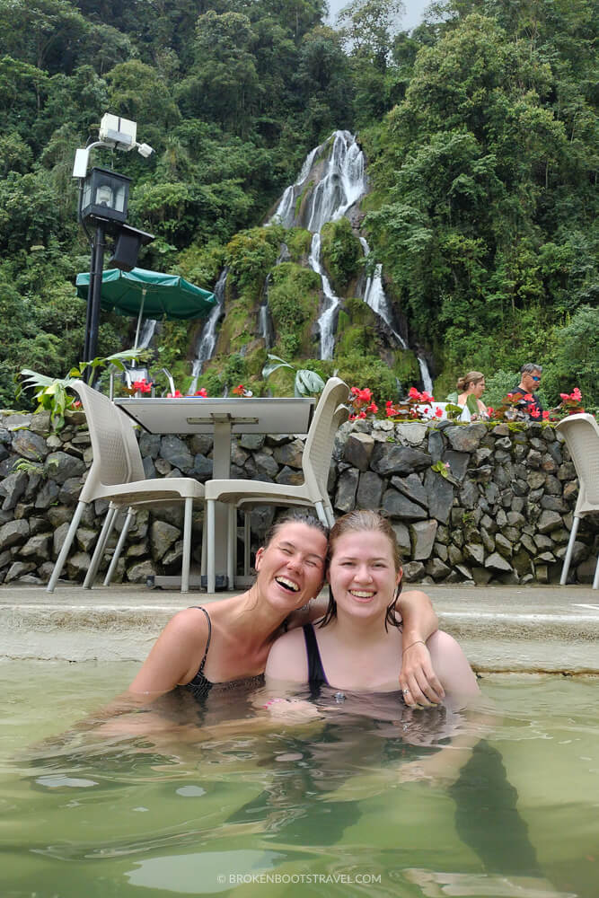 Two girls smiling in a hot spring with a waterfall behind them