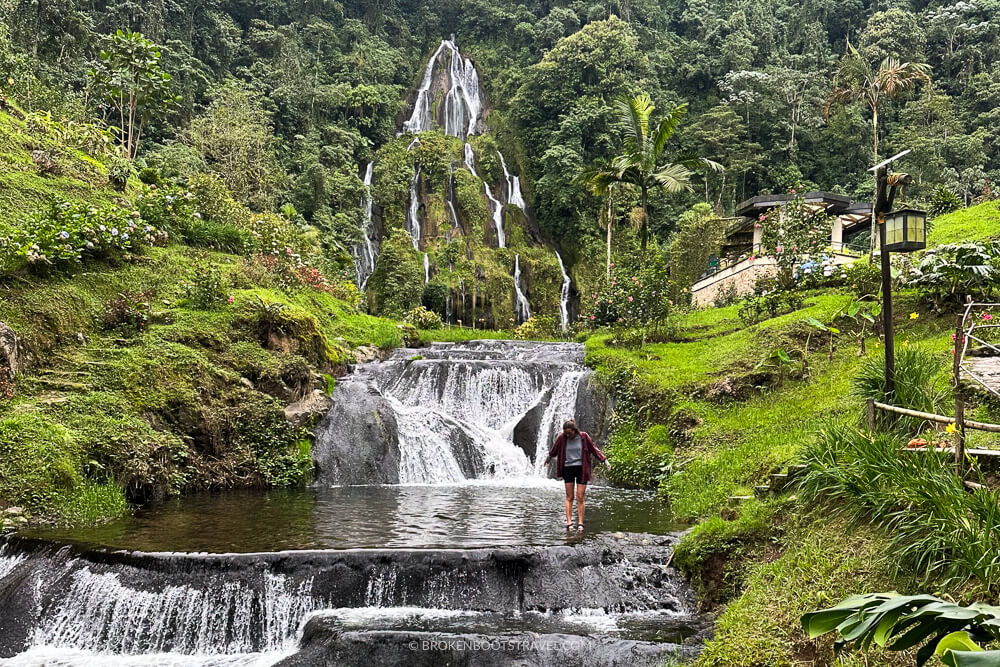 Girl standing in front of a waterfall with green mountains