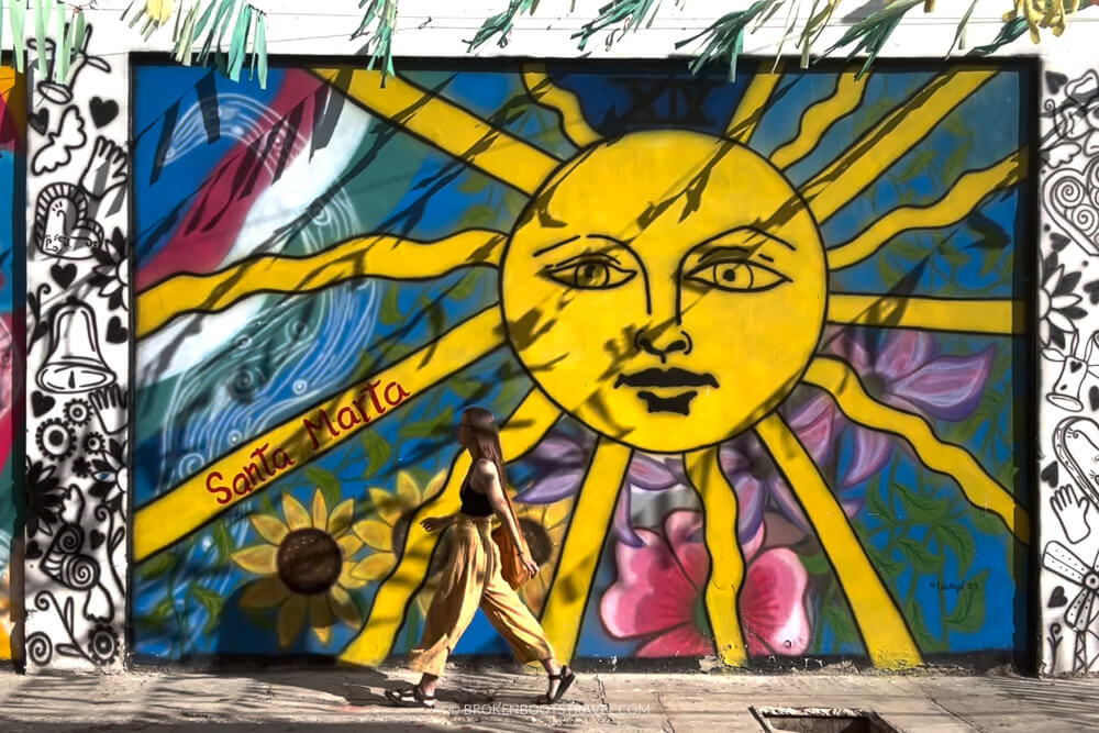 Girl walking in front of mural of sun in Santa Marta Colombian Coast