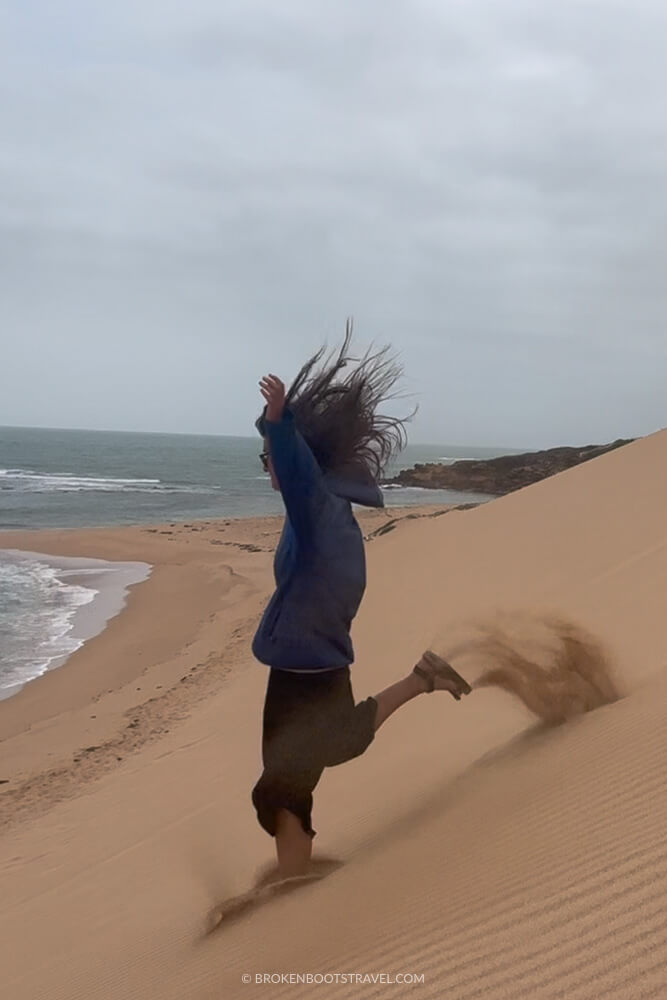 Girl in blue sweatshirt running down a large sand dune