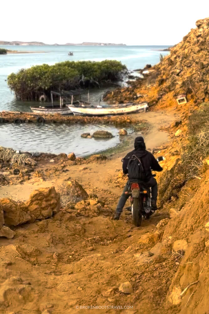 Man driving a motorbike down a sand road in front of water