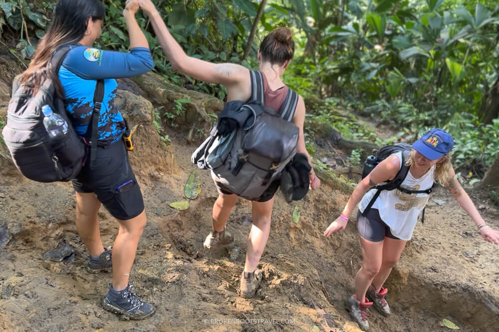 Three women hiking down a muddy path in the jungle