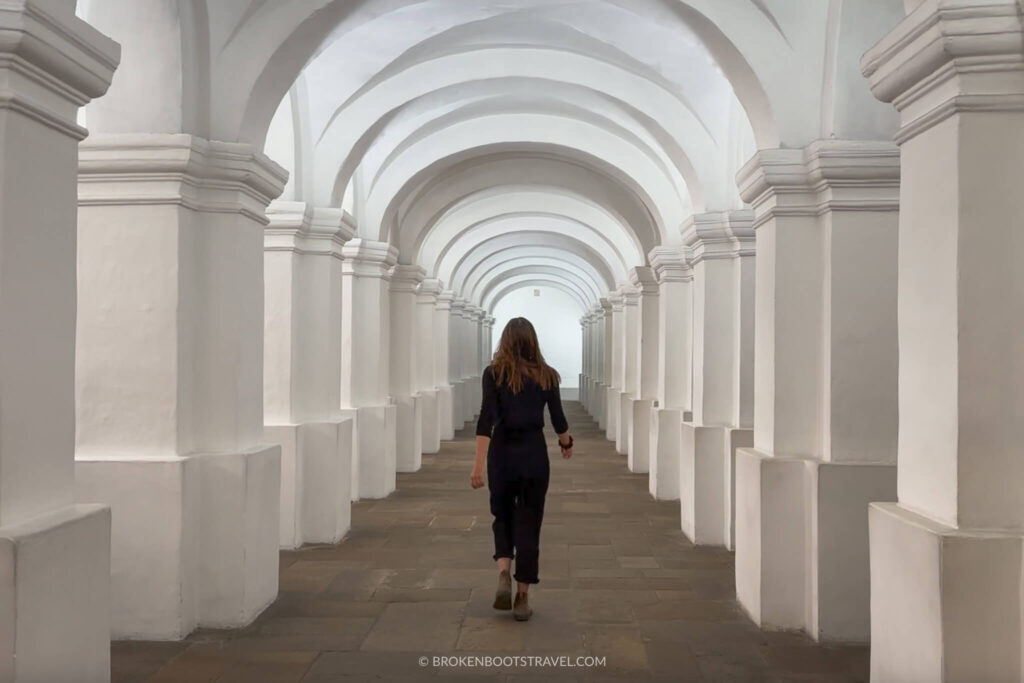 Girl in all black walking through white columns in a museum.