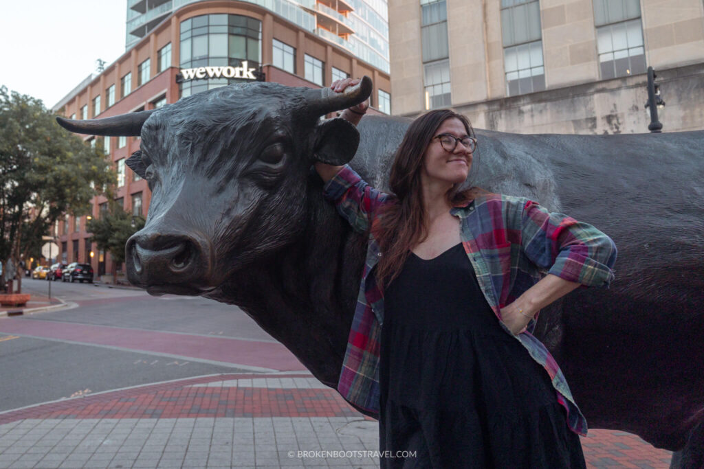 Girl smiling in front of a metal bull statue in Durham, North Carolina