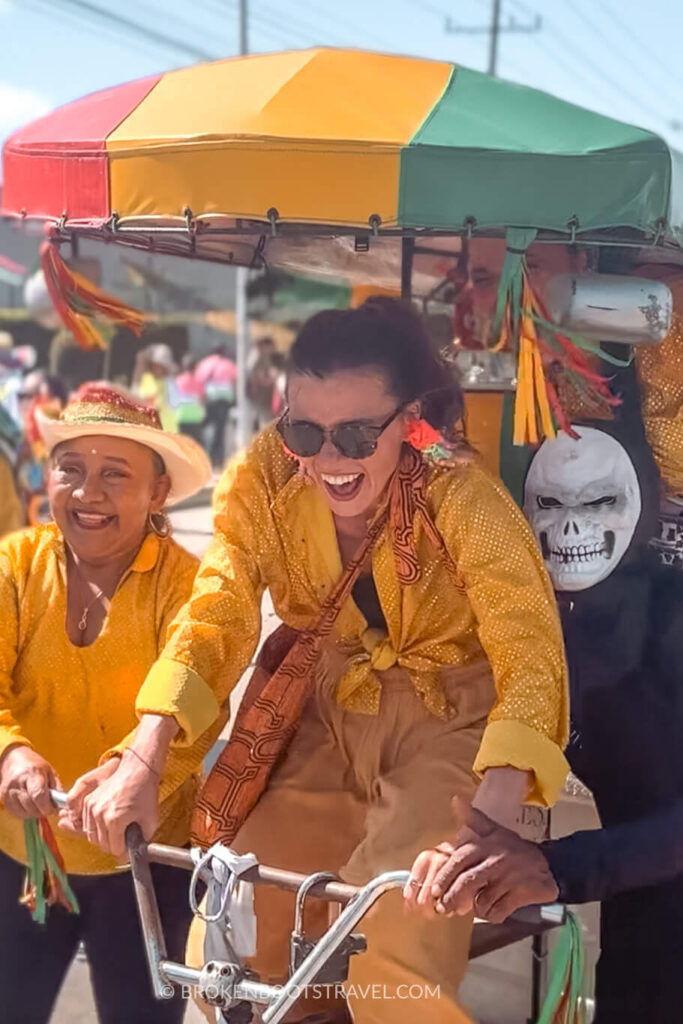 Girl in yellow shirt riding on a tricycle with a skeleton at Barranquilla Carnival 