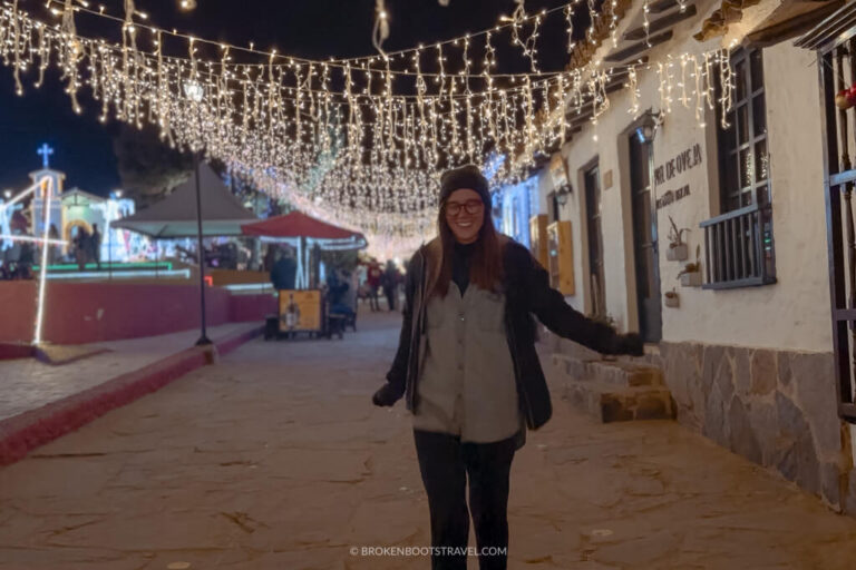 Girl in blue hat and blue jacket smiling under Christmas lights