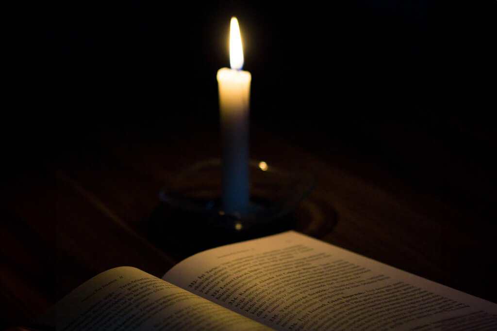 single candle lighting up a book against a black background