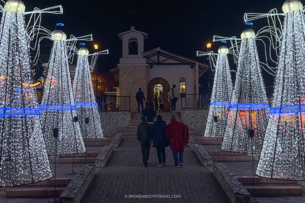 three people walking up to a church in between light up christmas trees