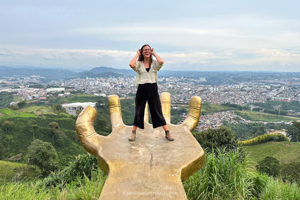 Girl in black pants and brown shirt standing on a gold hand with cityscape in the background, bogota medellin itinerary