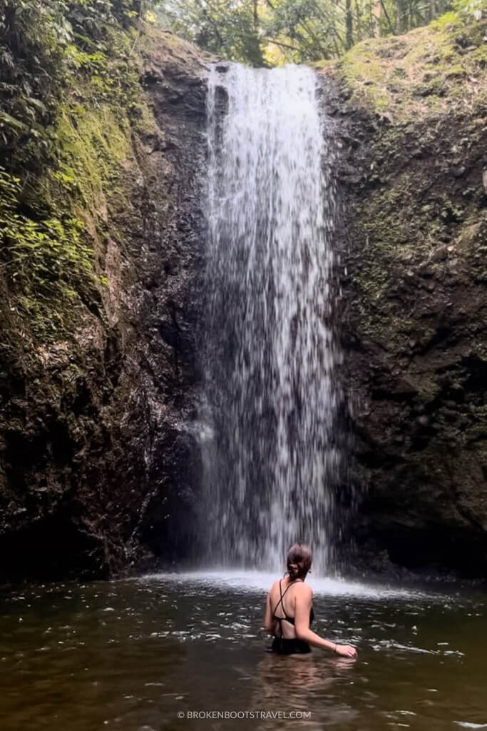 girl in black swimsuit standing in front of waterfall