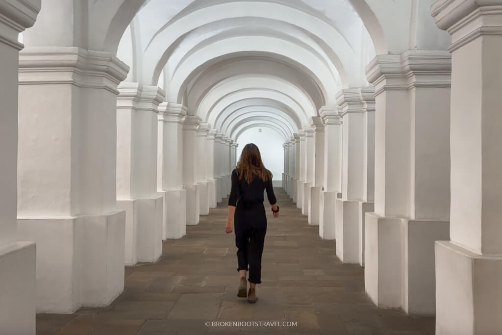 girl in all black walking down a hallway with white columns