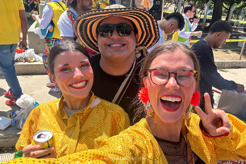 three people smiling at the camera, two women in yellow jackets and a man in all black with a black and white hat