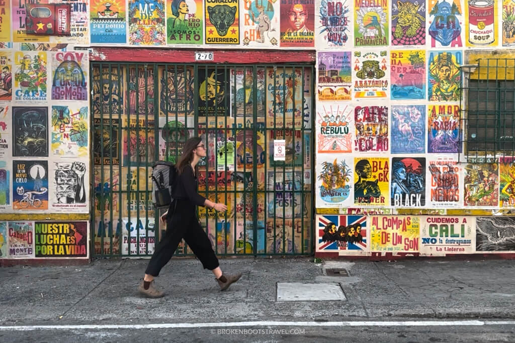 Girl in all black wearing backpack walking past wall of colorful posters