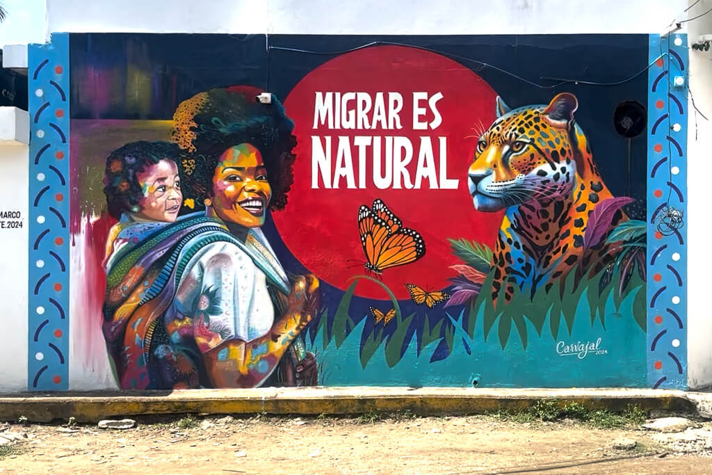 Mural showing a woman carrying a baby and the text "Migrar es Natural"