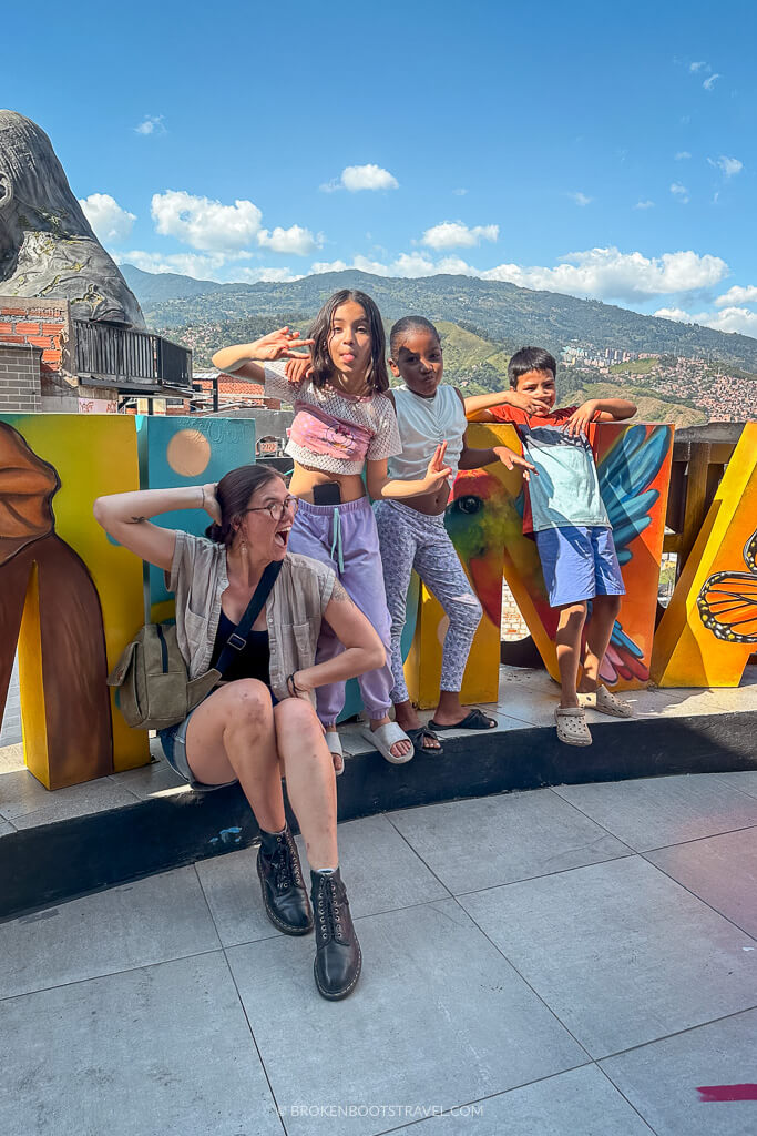 Four people pose in from of a sign reading "Medellin" with a city skyline in the background