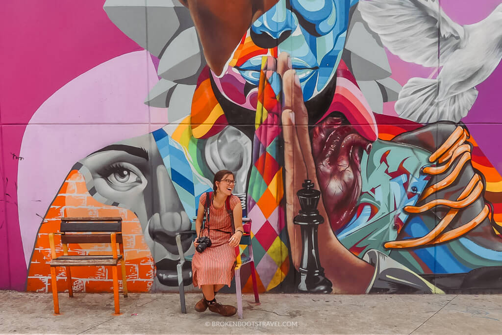 A girl in a red dress poses in front of a colorful mural