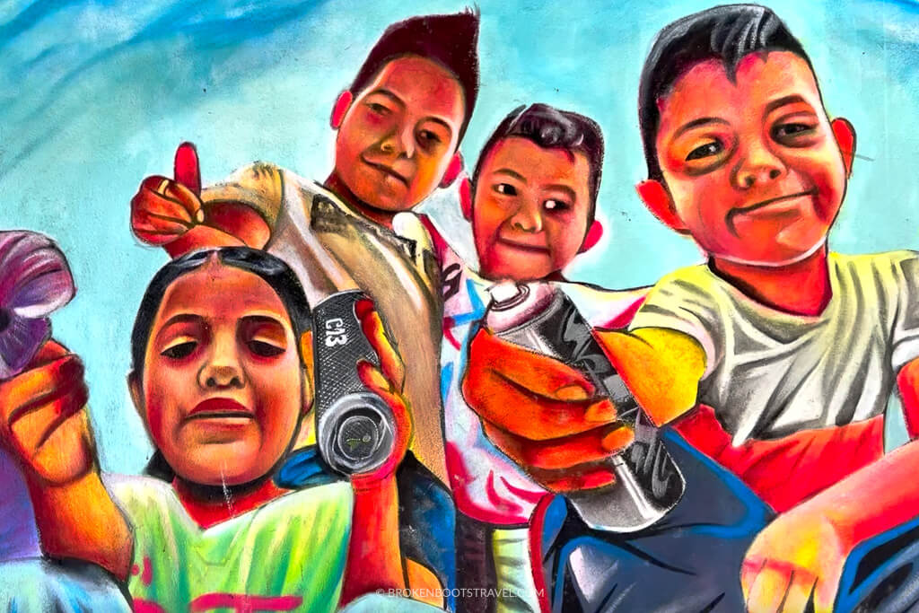 Mural of four children holding spray paint cans pointed at the viewer
