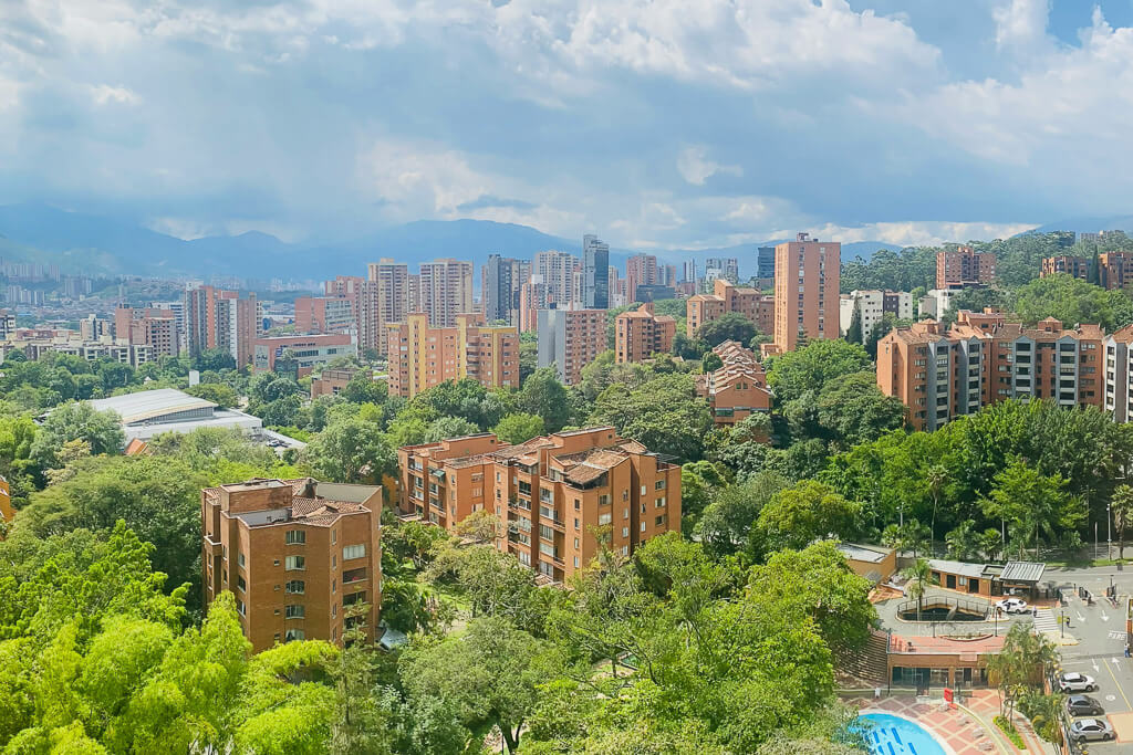 View of tall buildings amongst green trees with mountains in the background
