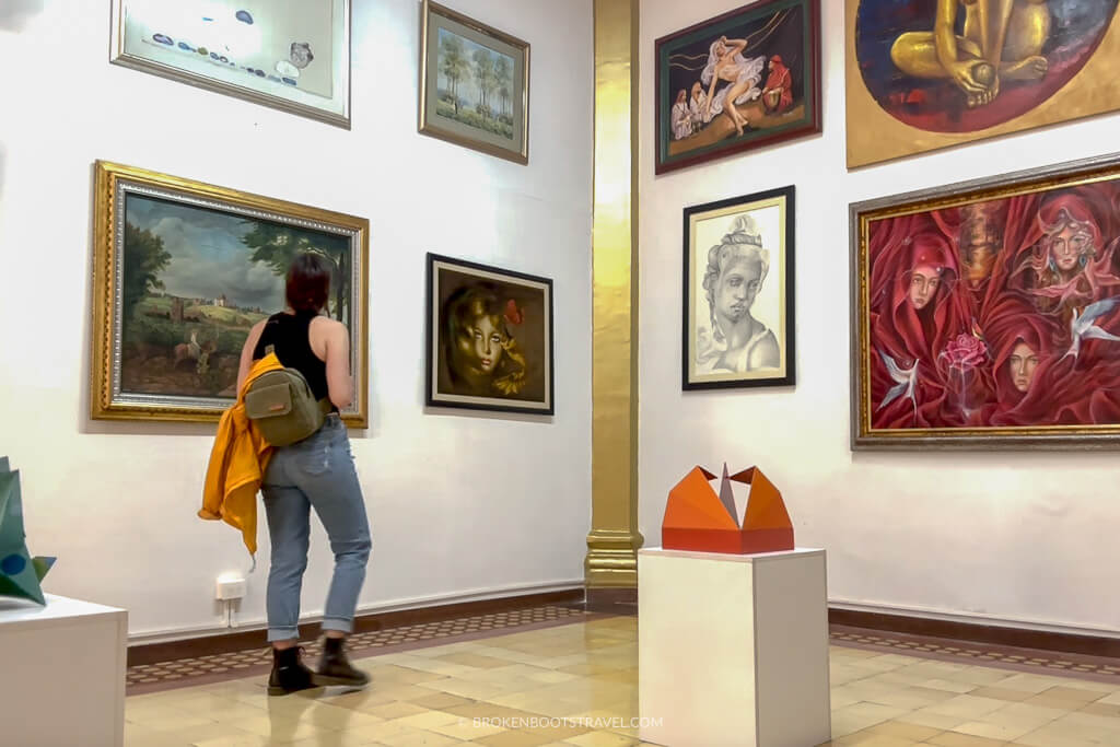 Girl in jeans and a black shirt looking at art hanging on the walls in El Palacio, Medellin