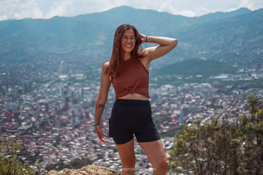 Girl in pink tank top poses in front of Medellín skyline and mountains