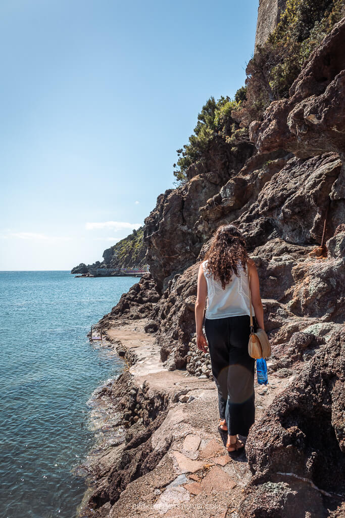 Girl in white shirt and black pants walking along rocky cliff