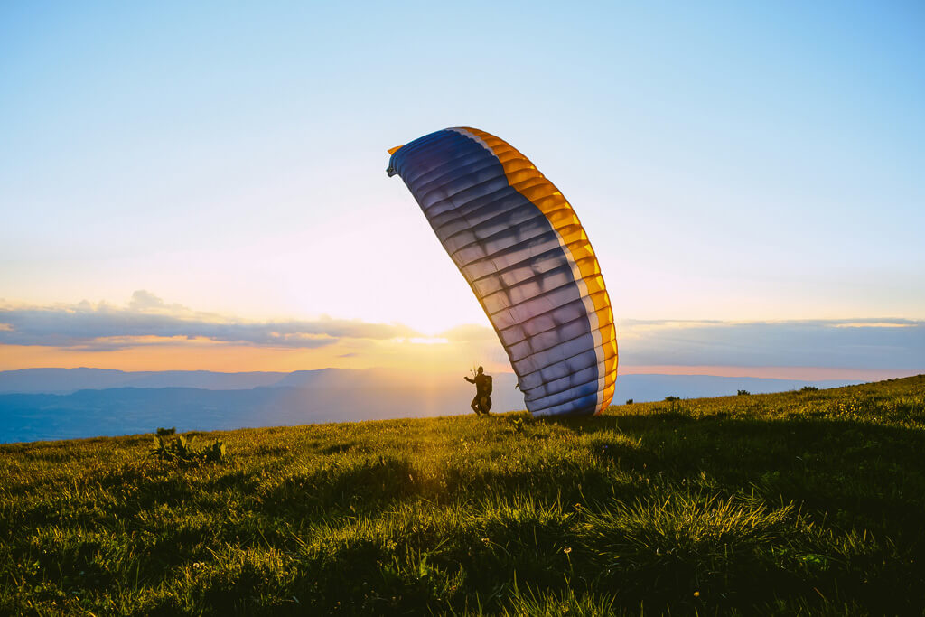 A man paragliding over mountains at sunrise