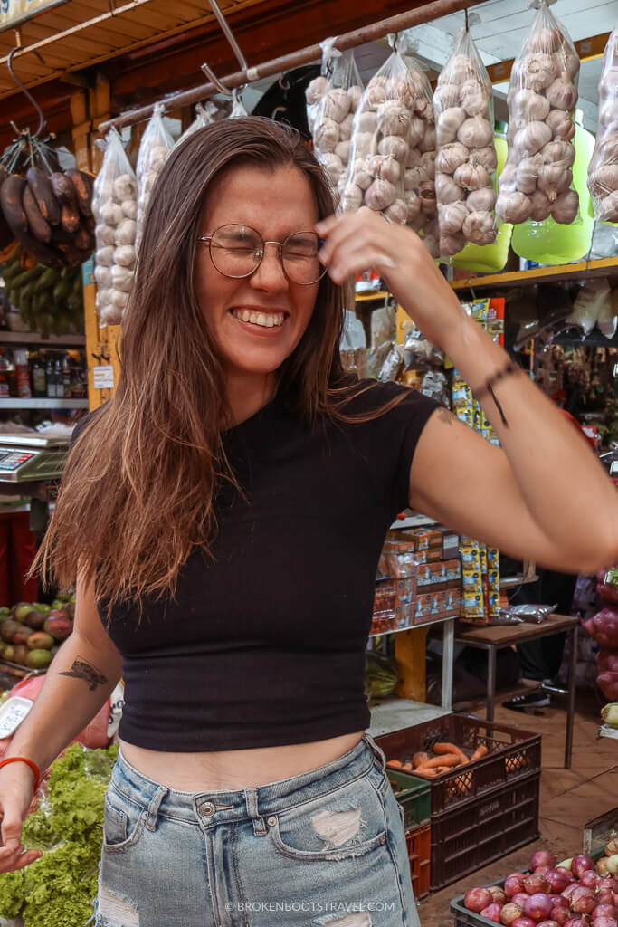 Woman in a black shirt and jeans smiling in front of rows of fruit and vegetables