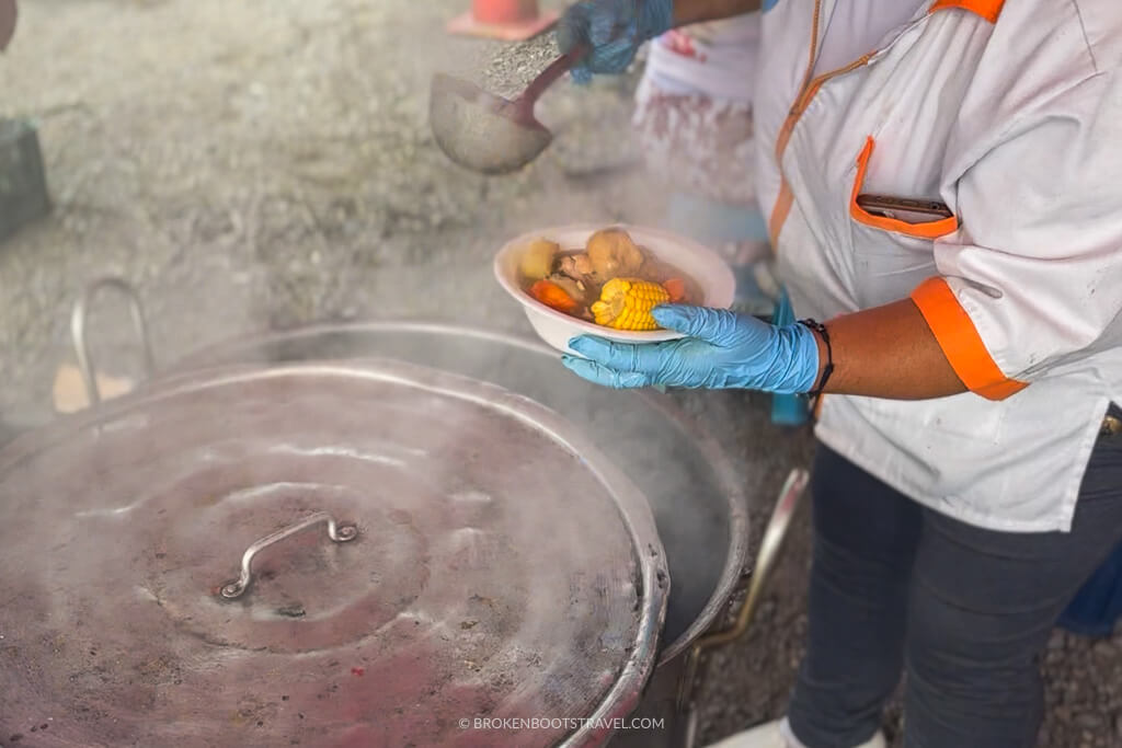 Hands wearing blue plastic gloves serving sancocho on the side of the road