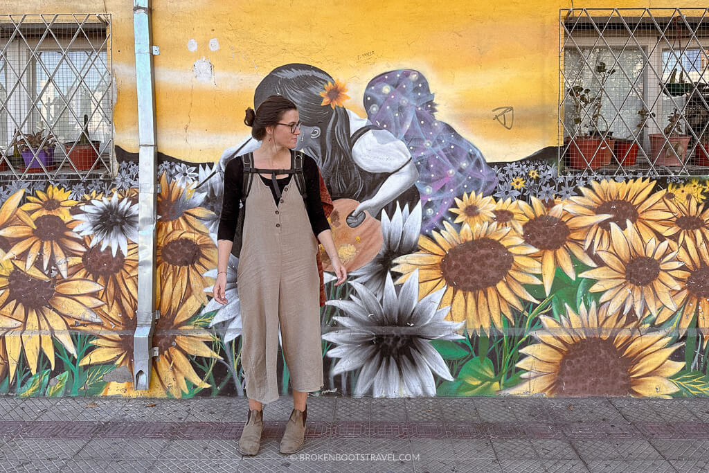 Girl in black shirt and brown overalls standing in front of sunflower mural