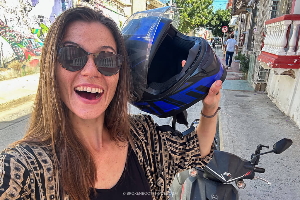 Girl in sunglasses taking a selfie and holding up a blue motorcycle helmet