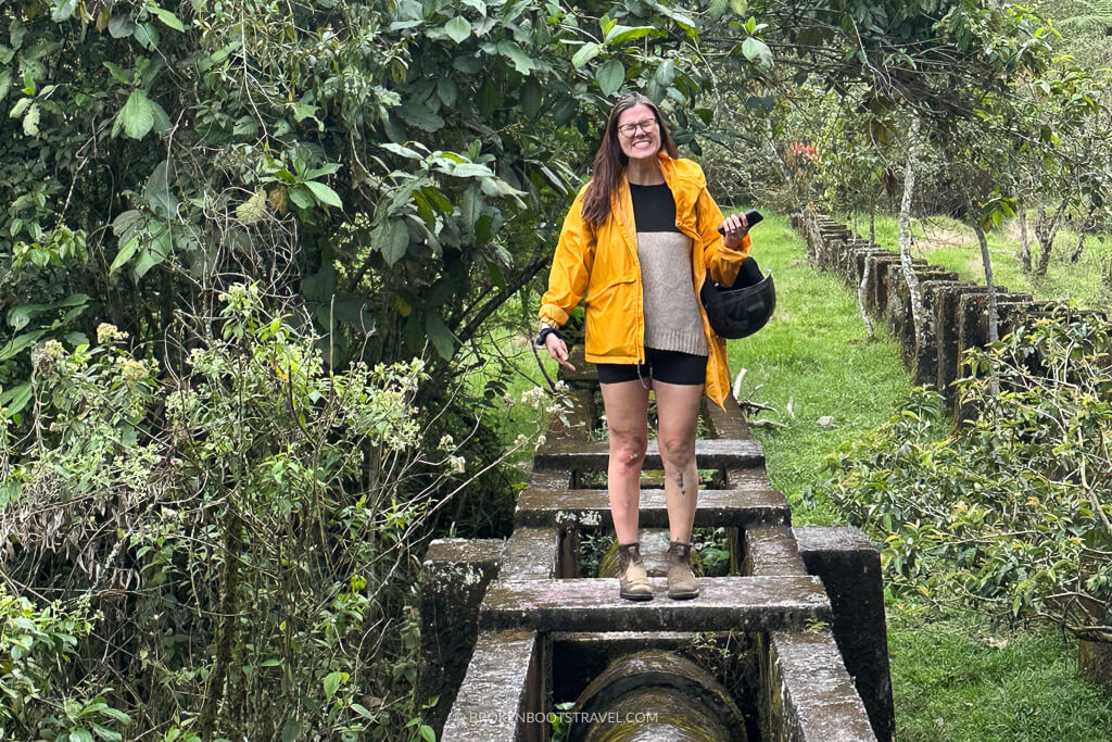 Girl in yellow rainjacket standing on a bridge in front of greenery