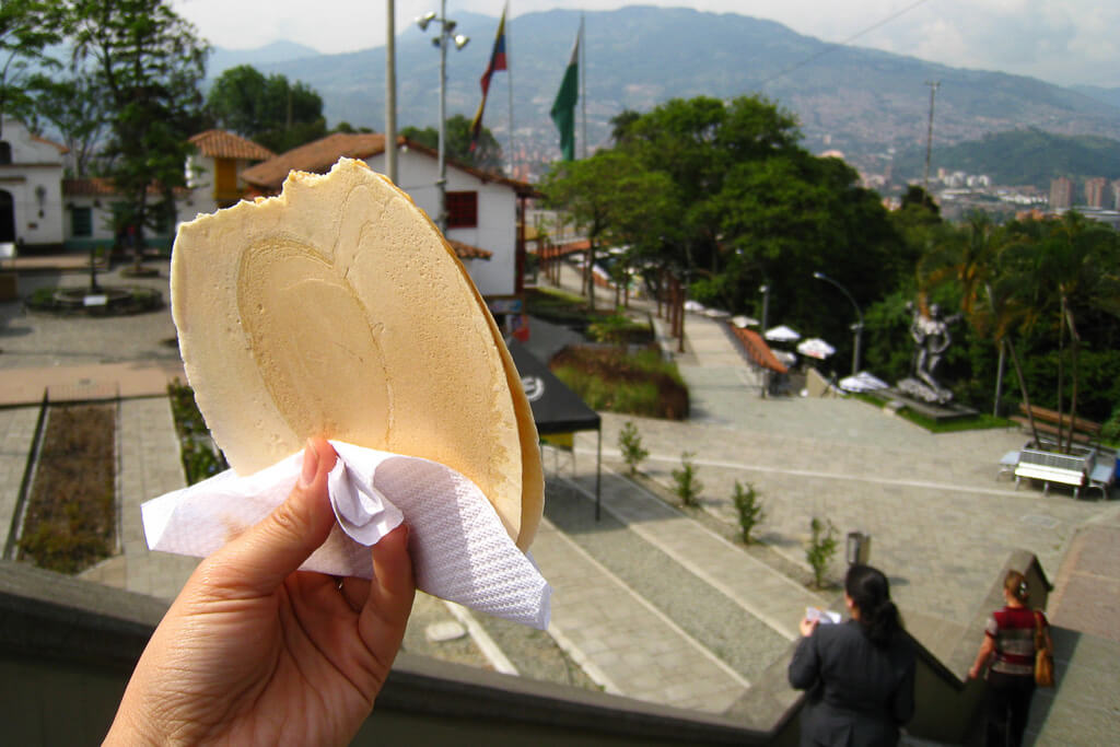 Hand holding an oblea in front of Medellín skyline