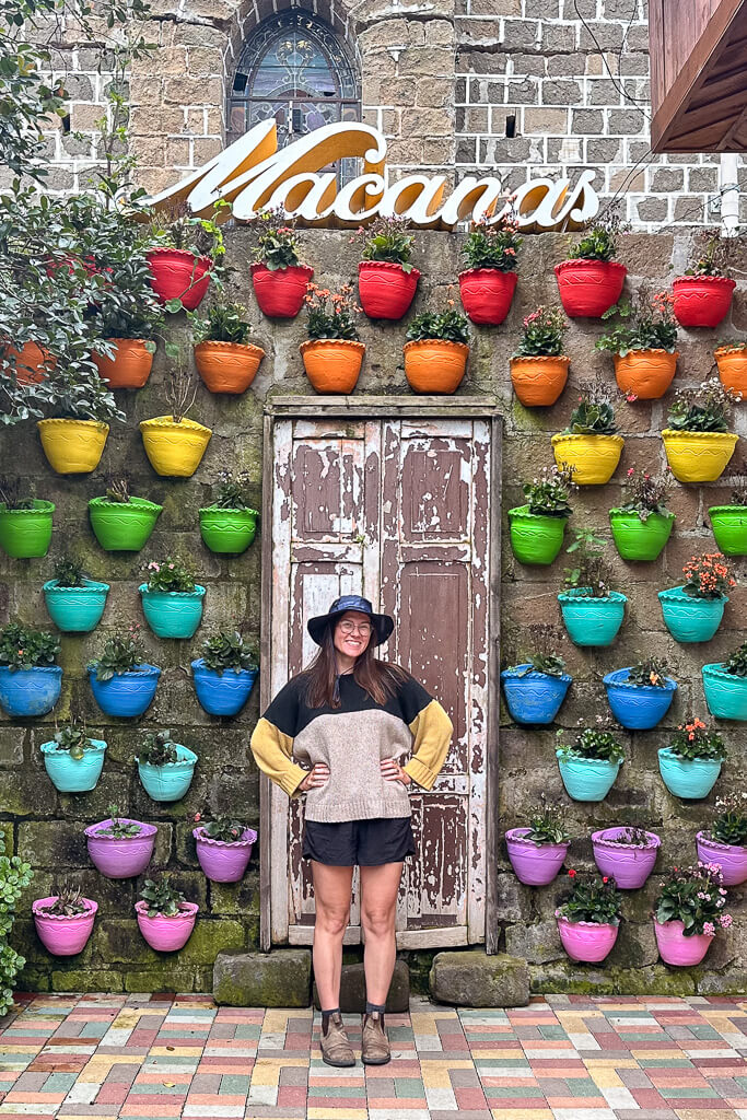 Girl in hat standing in front of a wall of colorful pots with "Macanas" Sign