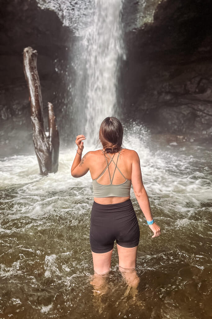 Girl looking at a waterfall in a cave wearing a green top and black shorts
