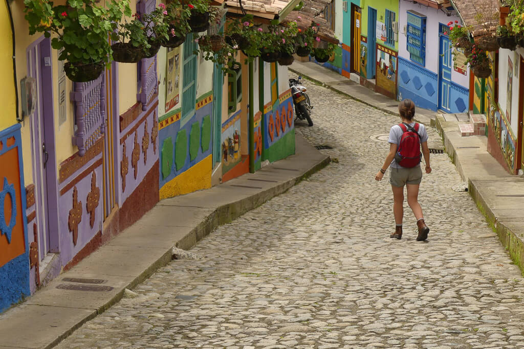 Girl with red backpack walking down colorful street of Guatape, Colombia