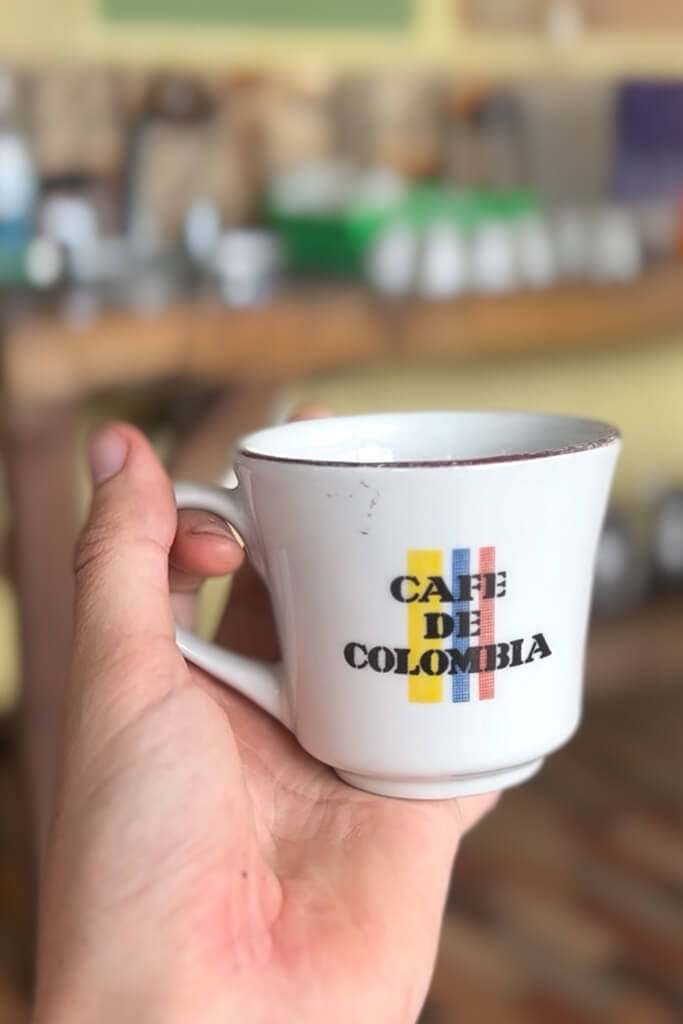 Hand holding a white cup saying "Cafe de Colombia"