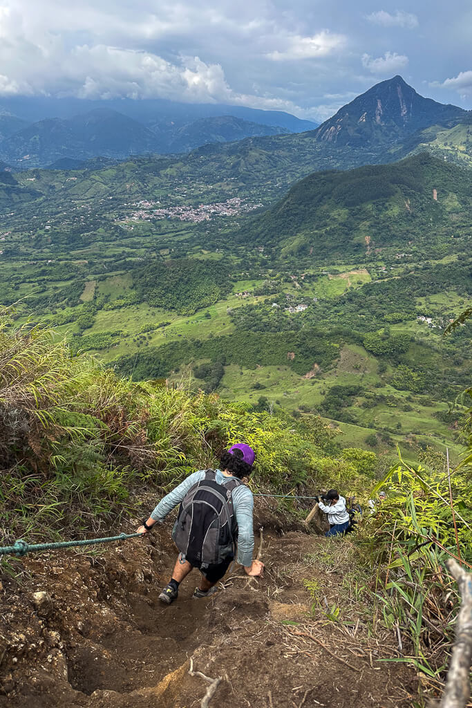 Man in purple hat climbing down a dirt path with mountains in the background