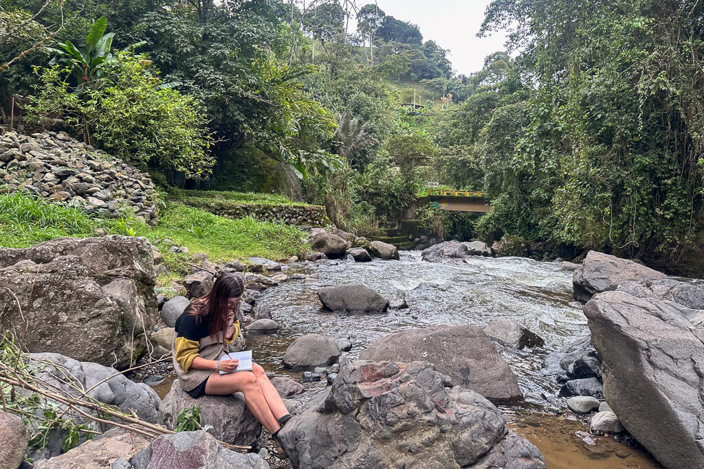 Girl in yellow sweater journaling beside the river