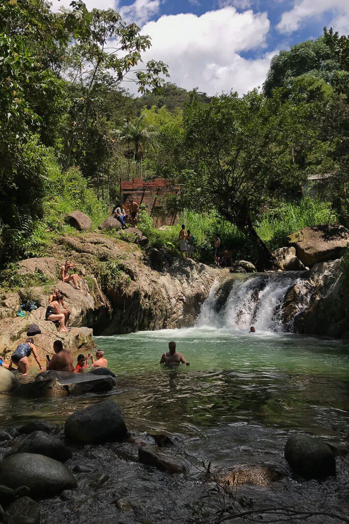 People swimming in a waterfall in front of green trees