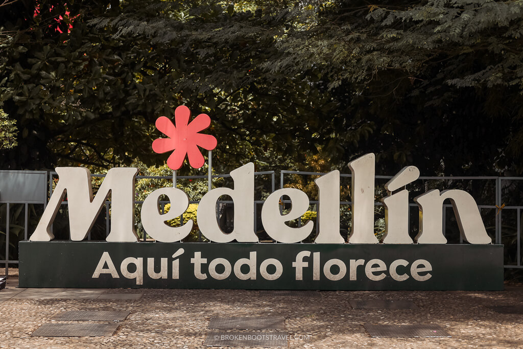 Sign reading "Medellín, Aquí todo florece" in front of green trees
