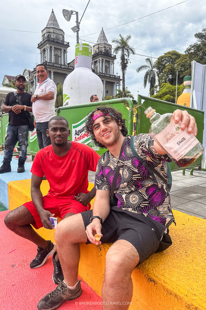 Two people smiling and holding a bottle of viche in front of the Quibdó Cathedral