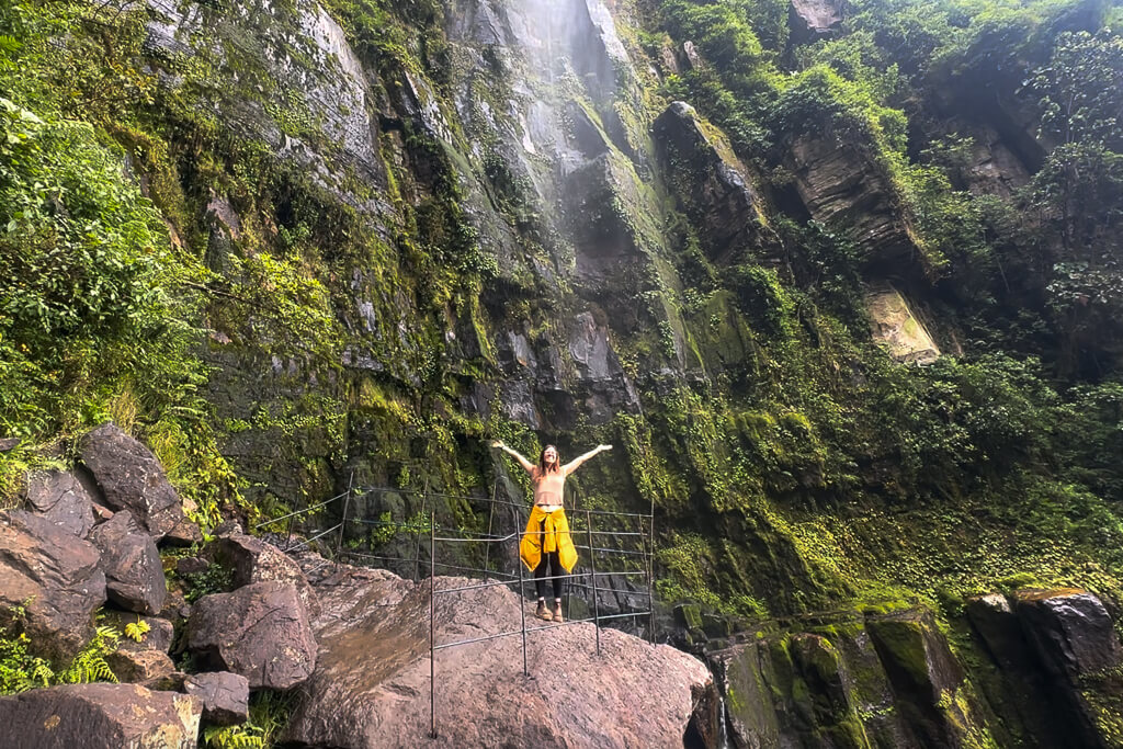 Girl in yellow jacket posing in front of waterfall